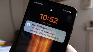Eine betrügerische SMS auf einem Smartphone-Display zu einer angeblichen Paketsendung enthält einen verdächtigen Link. 