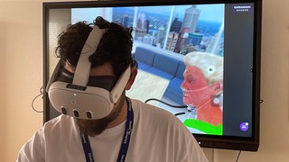 Ein Auszubildender der Pflege im Klinikum Worms trägt eine VR-Brille. Auf dem Bildschirm sieht man, was er Auszubildende in der Brille sieht.