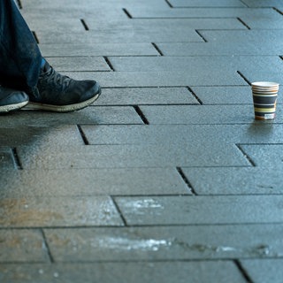 Füße eines Obdachlsoen, der einen Becher für Spenden aufgestellt hat. In Bad Kreuznach ist ein 13-Jähriger ermittelt worden, der einen Wohnsitzlosen mit einer Glasflasche angegriffen und verletzt haben soll