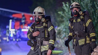 Feuerwehrleute stehen im Dunklen vor einem Löschwagen (Symbol). Feuerwehrleute (Symbol). Bei der Berufsfeuerwehr Mainz ist es nun möglich eine Ausbildung zu machen ohne vorher eine Berufsausbildung abgeschlossen zu haben. 