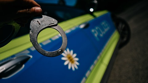 Ein Streifenwagen, ein Polizist mit Handschellen (Symbolbild): In Mainz hat die Polizei einen Mann fesgenommen, der Frauen sexuell belästigt, Gäste bedroht und sich mit der Polizei angelegt hat. 