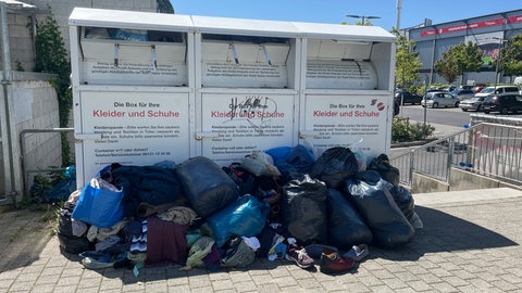 Vor den Altkleider-Containern stappeln sich Säcke mit Kleidungsstücken