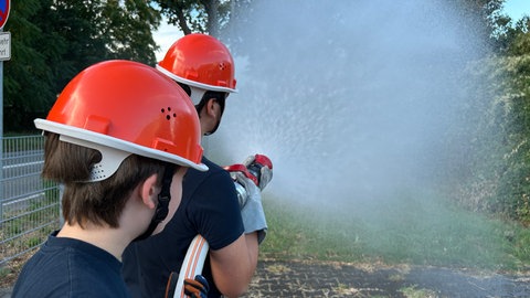 Zwei Jugendliche der Laubenheimer Jugendfeuerwehr halten einen Schlauch, aus dem Wasser spritzt. Hier werden schon früh Löscheinsätze geübt. 