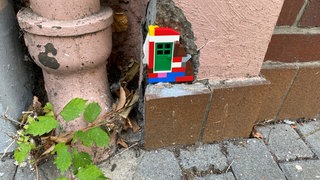An einem Haus ist etwas Putz abgebröckelt. In die Lücke wurde ein kleines Bauwerk aus Legosteinen mit einer grünen Tür eingesetzt.
