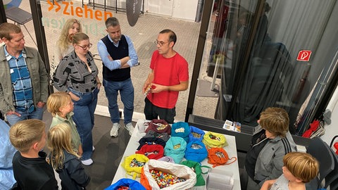 Jan Vormann steht inmitten einer Gruppe Menschen, auf dem Tisch vor ihm Legosteine in größeren und kleineren Säcken und Tüten.