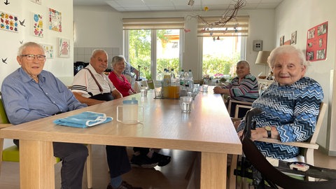 Die Bewohnerinnen und Bewohner der WG für Menschen mit Demenz in Alzey sitzen gemeinsam an einem langen Tisch.
