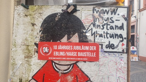 Anwohner haben einen Aufkleber auf den Bauzaun des baufälligen Hauses in der Augustinerstraße in Mainz geklebt mit der Aufschrift: "10-jähriges Jubiläum der Ebling Haase Baustelle".