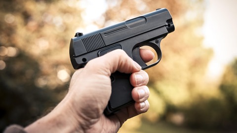 Eine männliche Hand hält eine Schusswaffe: Vor dem Mainzer Landgericht muss sich ein Mann wegen mehrerer Raubüberfälle vernatworten. Er soll sie auf einem Motorroller mit einer Schuswaffe in der Hand begangen haben. (Symbol)