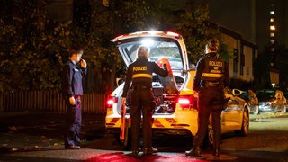 Ein Polizist und zwei Polizistinnen stehen an einem Polizeiwagen in Mainz-Gonsenheim, nachdem ein Unbekannter einen falschen Notruf abgesetzt hat.
