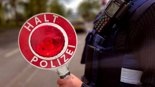 Eine Polizisten hält eine "Halt"-Kelle hoch. In Mainz hat die Polizei einen 18-Jährigen gestoppt, der auf einem getunten Motorroller unterwegs war. 
