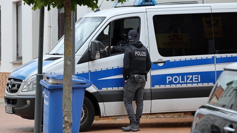 Ein Polizeiwagen und zwei Polizisten warten vor einem Haus.