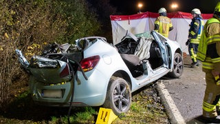 Ein beim Unfall zerstörtes Auto steht am Straßenrand, dahinter steht ein Sichtschutz der Feuerwehr.