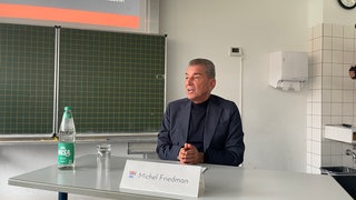 Michel Friedman sitzt an einem Pult. Der Publizist hat das Otto-Schott-Gymnasium im Rahmen des ARD-Jugendmedientags besucht. 