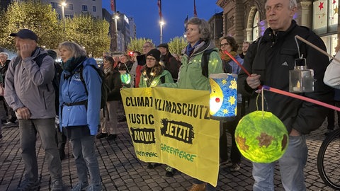 Männer und Frauen demonstrieren mit Transparenten und Laternen für den Klimaschutz.