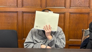 Ein Mann hälte sich einen Aktenordner vor Gesicht: Das Landgericht Mainz hat den Mann heute wegen mehrere Raubüberfälle zu vier Jahren und drei Monaten Haft verurteilt.