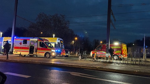 Eine Straßenbahn, ein Rettungswagen und ein Auto der Feuerwehr stehen an der Haltestelle Universität in Mainz. Jemand ist unter die Straßenbahn geraten