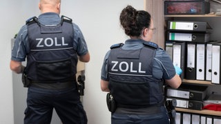 Zwei Zollbeamte durchsuchen ein Büro. (Symbolbild)