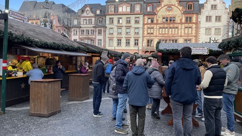 Menschen stehen vor Buden auf dem Mainzer Weihnachtsmarkt und essen und trinken
