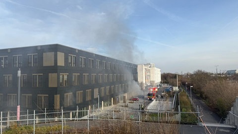 Rauch steigt aus einem große Gebäude: Brennende Autos in einer Tiefgarage sollen ein Feuer in dem Haus in Mainz-Gonsenheim ausgelöst haben.