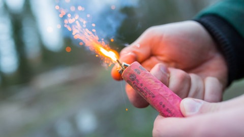 Eine Hand zündet einen Feuerwerkskörper an. (Symbolbild) In Bad Kreuznach hat ein Mann Feuerwerkskörper auf Frauen geworfen. 