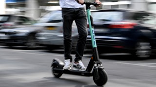 (Symbolbild) Ein E-Scooter Fahrer rast mit hoher Geschwindigkeit auf der Straße an parkenden Autos vorbei. 