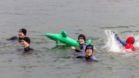 Männer und Frauen mit Polizei-Mützen schwimmen im Rhein, sie haben ein Gummikrokodil dabei.