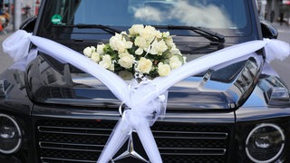 Ein großer Geländewagen steht geschmückt mit weißen Schleifen und Rosen bereit für einen Hochzeitskorso.