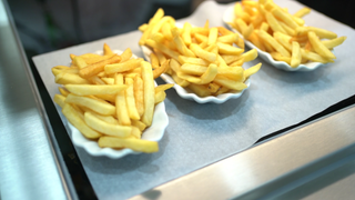 Drei kleine weiße Schälchen aus Porzellan mit Pommes stehen auf einer Theke.