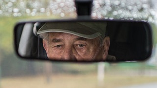 Ein älterer Autofahrer blickt in den Rückspiegel: Ein 92-jähriger Mann hat in Mainz seine Ehefrau gesucht 