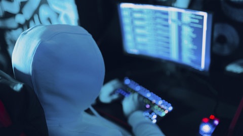 Ein Hacker mit Kapuze arbeitet an der Codeseite auf dem PC. (Symbol) 