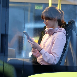 Eine Frau mit Kopfhörern hält im Bus ihr Handy in der Hand.