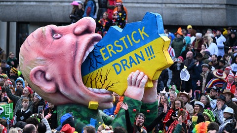 Bei diesem Mottowagen von Jacques Tilly sieht man Russlands Präsidenten Putin wie er den Mund aufreißt und versucht, die Ukraine zu verschlingen. Dort steht: "Erstick dran".