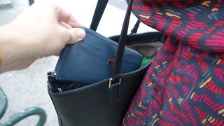 Ein Mann greift in die Tasche einer Passantin und zieht ihren Geldbeutel heraus.