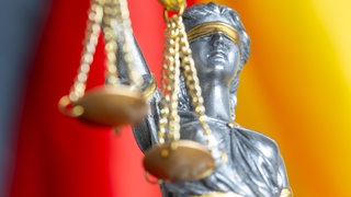 Nahaufnahme einer Justitia vor der Flagge von Deutschland (Symbolbild). Ein Gericht hat entschieden, dass auch die AfD zu einer Wahldebatte in Mainz eingeladen werden muss.