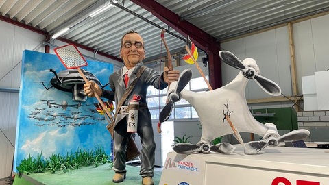 Verteidigungsminister Boris Pistorius (SPD) schießt Drohnen mit Pfeil und Bogen ab. Die Zugnummer 27 zeigt wie schwer der Bundeswehr die Verteidigung fällt, wenn die Mittel nicht da sind.  