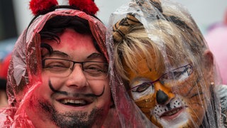 Ein Teufel und eine Tigerin im Regenponcho bei der Fastnacht in Mainz. Am Rosenmontag 2026 gibt es Schnee, Sonne und Regen