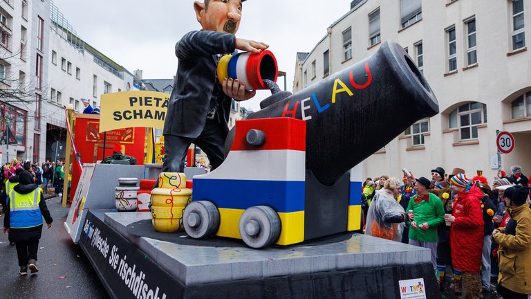 Motivwagen beim Mainzer Rosenmontagszug: Bestattung auf "meenzerich" - eine Konfettikanone wird mit Asche befüllt.