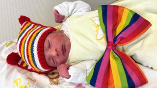 Ein neugeborener Säugling mit vierfarbbunter Mütze. Der Junge kam im Marienhaus Klinikum Mainz zur Welt und ist das erste Rosenmontagsbaby 2026 