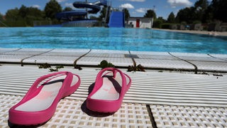 Zwei rosafarbene Badeschuhe stehen vor dem Beckenrand eines Freibades. Zwei Jugendliche haben eine 12-Jährige im Freibad sexuell missbraucht. (Symbolbild)