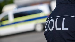 Ein Zoll-Mitarbeiter vor einem Polizeiwagen. 