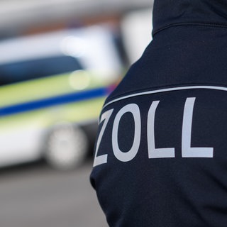 Ein Zoll-Mitarbeiter vor einem Polizeiwagen. 
