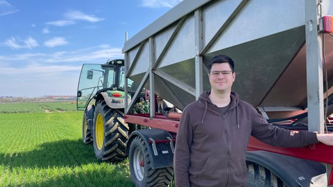 Ein junger Mann steht vor seinem Traktor auf einem grünen Acker