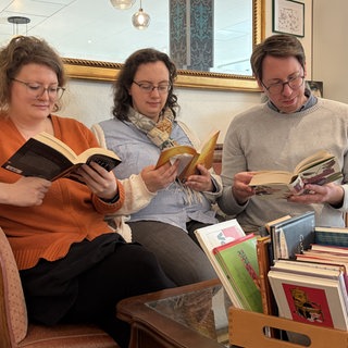 Ramona, Katrin und Dominik sitzen auf dem Sofa und lesen. Das ist der Silent Book Club von Mainz.  