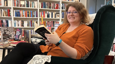 Ramona vom Silent Book Club sitzt im Sessel mit einem Buch in der Hand. 