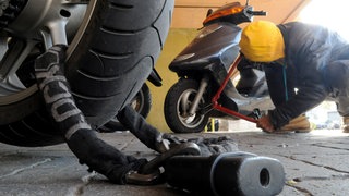 Ein Mann versucht einen Roller zu knacken. Rund um Mainz gab es mehrere Rollerdiebstähle (Symbolbild)