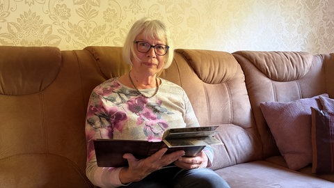 Doris Breyer sitzt mit einem Fotobuch von ihren Besuchen in Belarus auf einer Couch. 