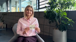 Die Tschernobyl-Zeitzeugin Nadiia Skopych sitzt auf einem Sessel und zeigt ein Foto mit dem neuen Haus ihrer Famile in die Kamera.