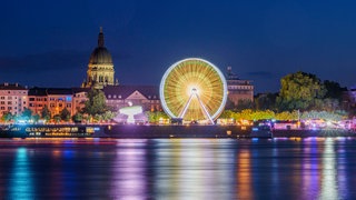 Am Rheinufer in Mainz steht beim Johannisfest ein Riesenrad, das nachts leuchtet. 