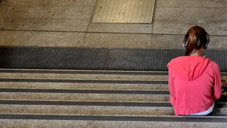 Ein Kind sitzt allein auf einer Treppe. Viele Kinder und Jugendliche sind einsam. Ein Sorgentelefon hilft. 