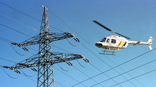 Ein Hubschrauber fliegt dicht über Stromleitungen: Die Mainzer Netze kontrollieren so die Leitungen (Symbolbild) 